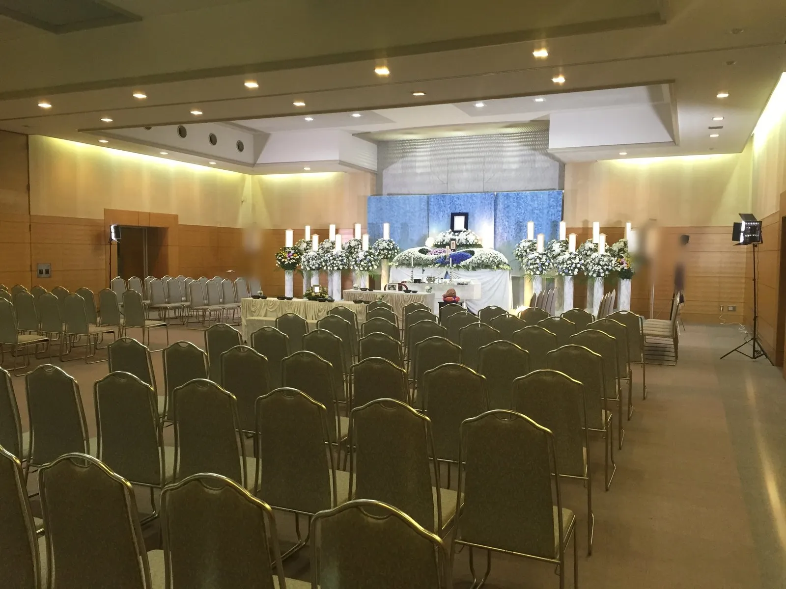 茅ヶ崎市斎場の告別式場。白と青の花の祭壇の前に、会葬者席の椅子が並ぶ